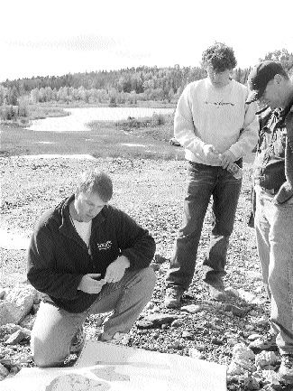 Ken Lapierre, Mustang Minerals' vice-president of exploration, kneeling (on waste rock from the Maskwa open pit) and James Moon, Senior Investment advisor with Standard Securities. The flooded ramp of the former Maskwa open pit is in the background.