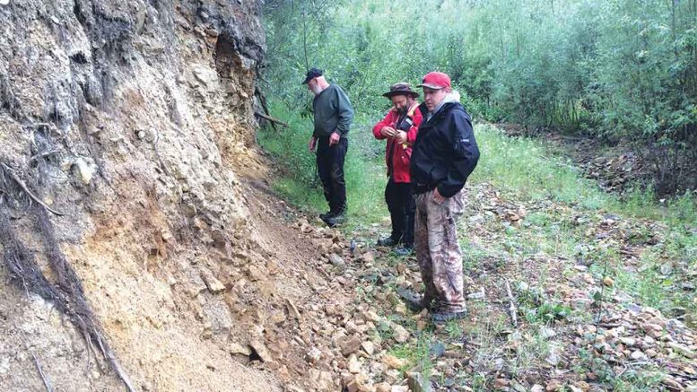 Triumph Gold’s vice-president of exploration Tony Barresi (centre) takes notes at an exposure of strongly altered rock on the margin of Triumph’s Revenue diatreme in Whirlwind Creek in the Yukon, with placer miner John Gow (left) and Kyle Cashin of the Little Salmon Carmacks First Nation. Credit: Triumph Gold.