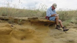 USGS geologist Bradley Van Gosen taking notes while sitting on top of a uranium-bearing calcrete outcrop in the southern United States. Credit: USGS.